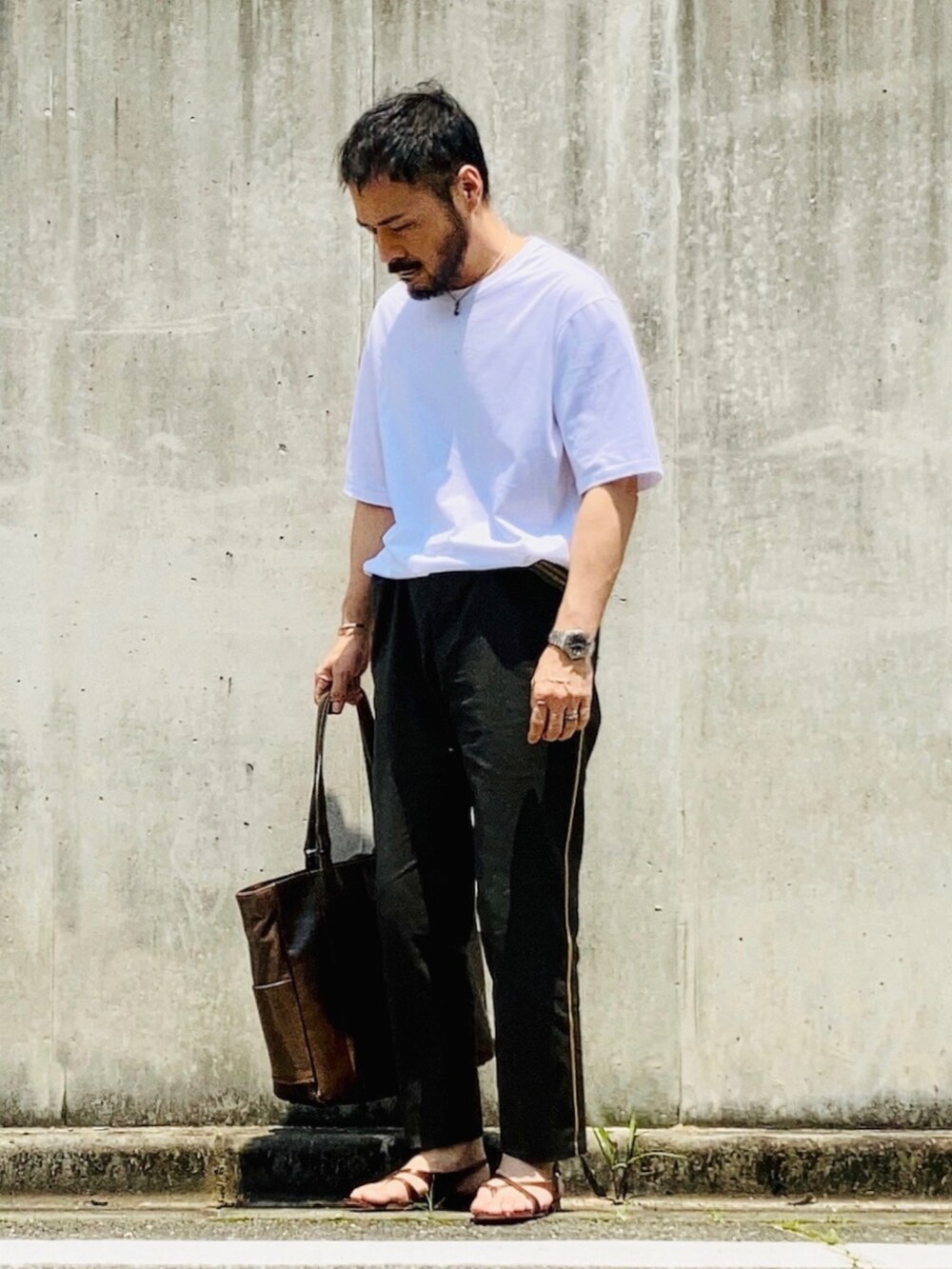 ホワイト系のTシャツ/カットソー、グリーン系のスラックス、ブラウン系のサンダルを着用したメンズの春コーディネートの2枚目の写真