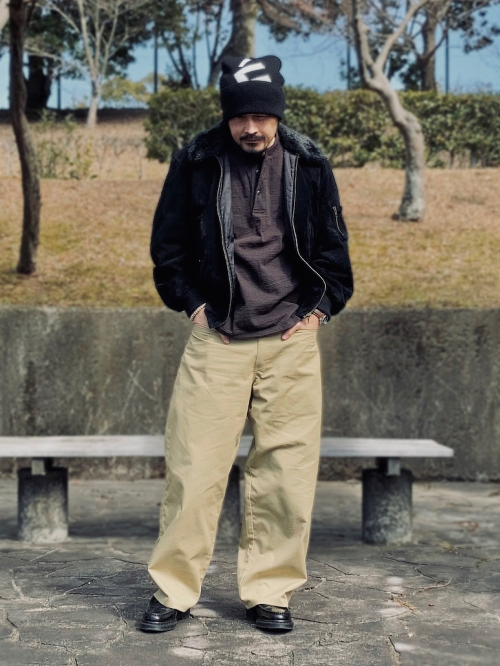 ブラック系のブルゾン、ブラウン系のTシャツ/カットソー、ベージュ系のチノパンツを着用したメンズの冬コーディネートの4枚目の写真