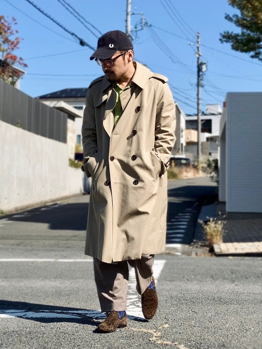 グリーン系のポロシャツ、ベージュ系のトレンチコート、ブラウン系のスラックスを着用したメンズの秋コーディネートの2枚目の写真