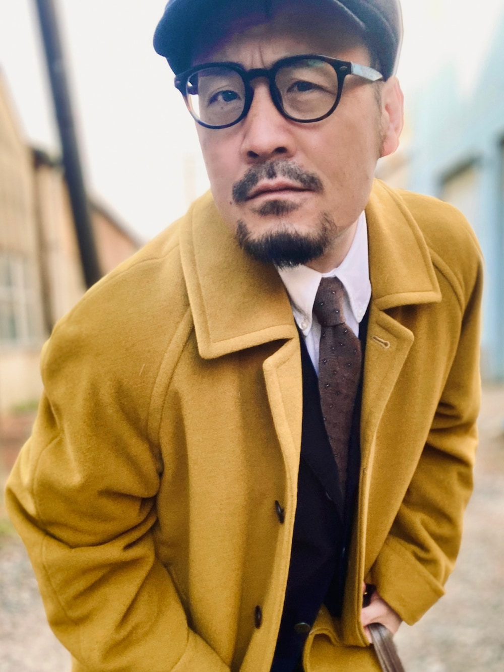 イエロー系のステンカラーコート、グリーン系のその他パンツ、ブラウン系のドレスシューズを着用したメンズの冬コーディネートの3枚目の写真