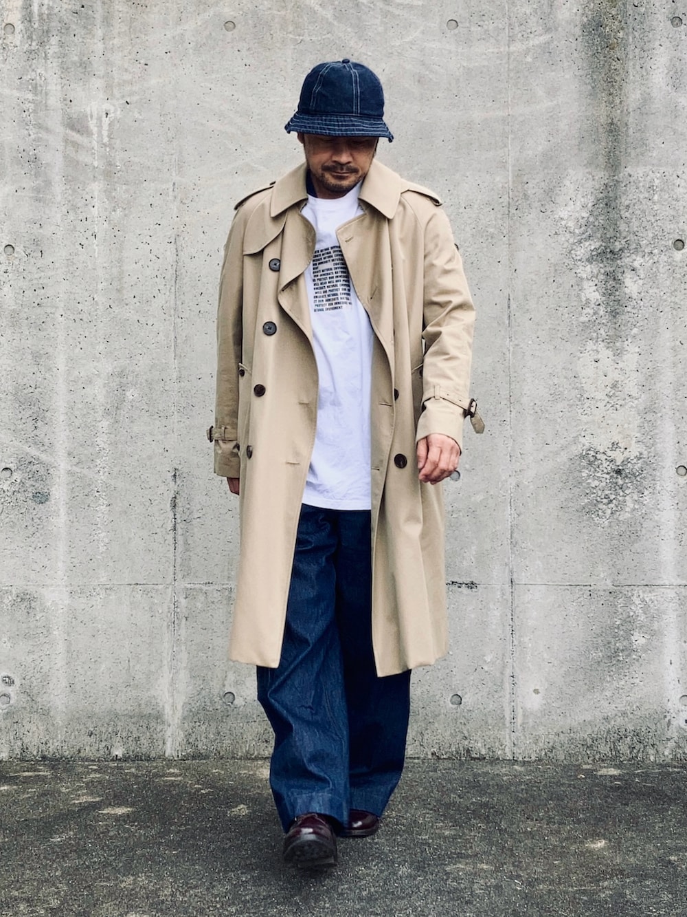 ホワイト系のTシャツ/カットソー、ベージュ系のトレンチコート、ブルー系のデニムパンツを着用したメンズの春コーディネートの2枚目の写真