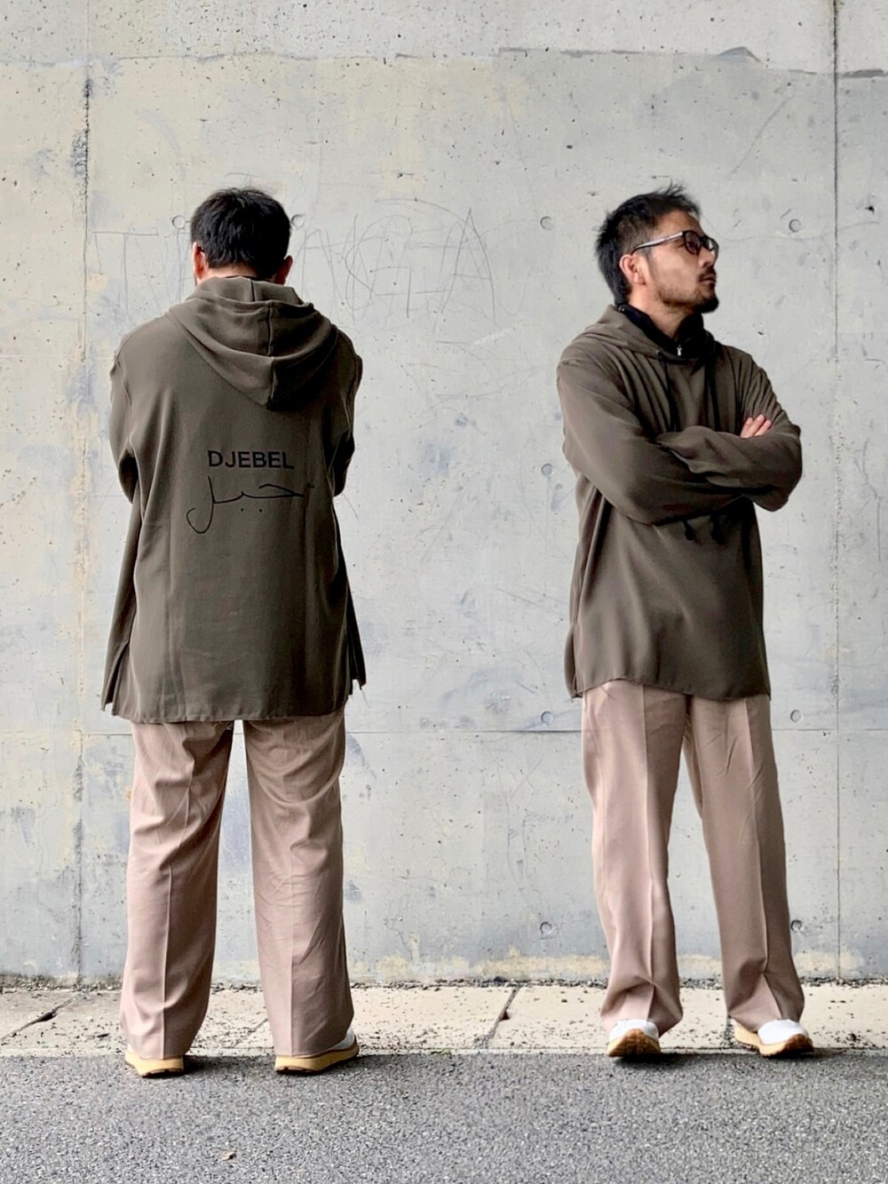 ブラック系のニット/セーター、グレー系のパーカー、ベージュ系のスラックスを着用したメンズの春コーディネートの2枚目の写真