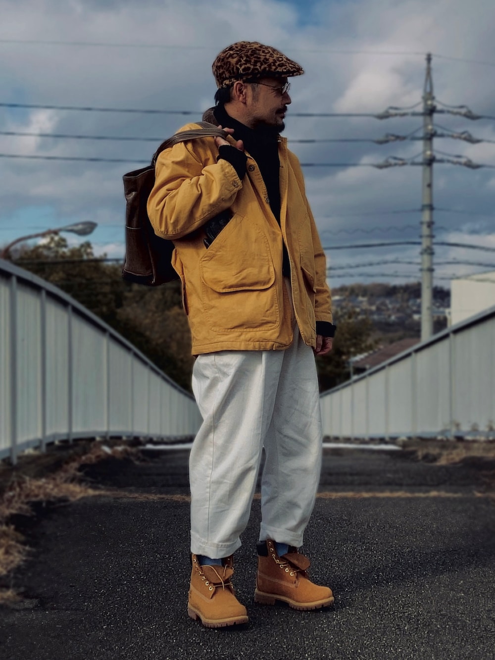 ブラック系のニット/セーター、イエロー系のカバーオール、ホワイト系のスラックスを着用したメンズの冬コーディネートの3枚目の写真