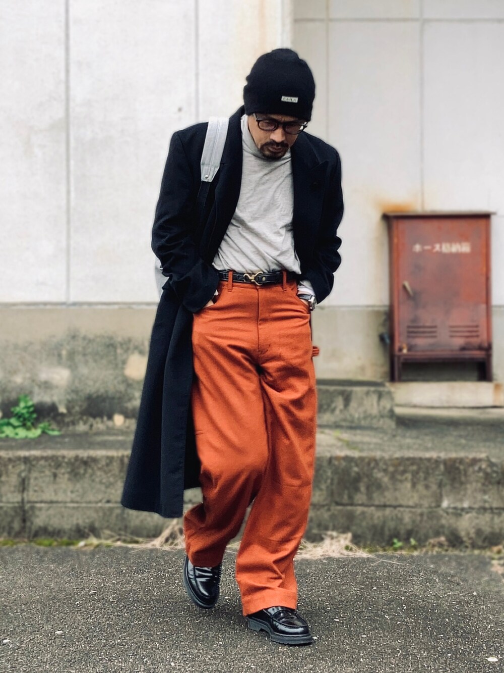 グレー系のTシャツ/カットソー、ブラック系のチェスターコート、オレンジ系のカーゴパンツを着用したメンズの冬コーディネートの3枚目の写真