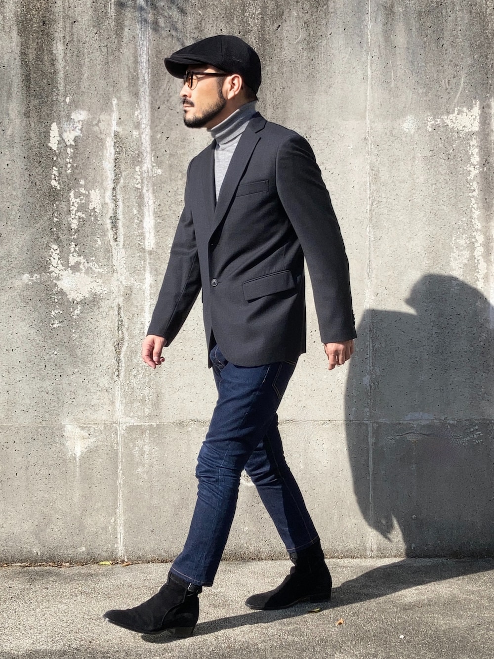 グレー系のテーラードジャケット、ブラック系のブーツ、ブルー系のデニムパンツを着用したメンズの秋コーディネートの4枚目の写真