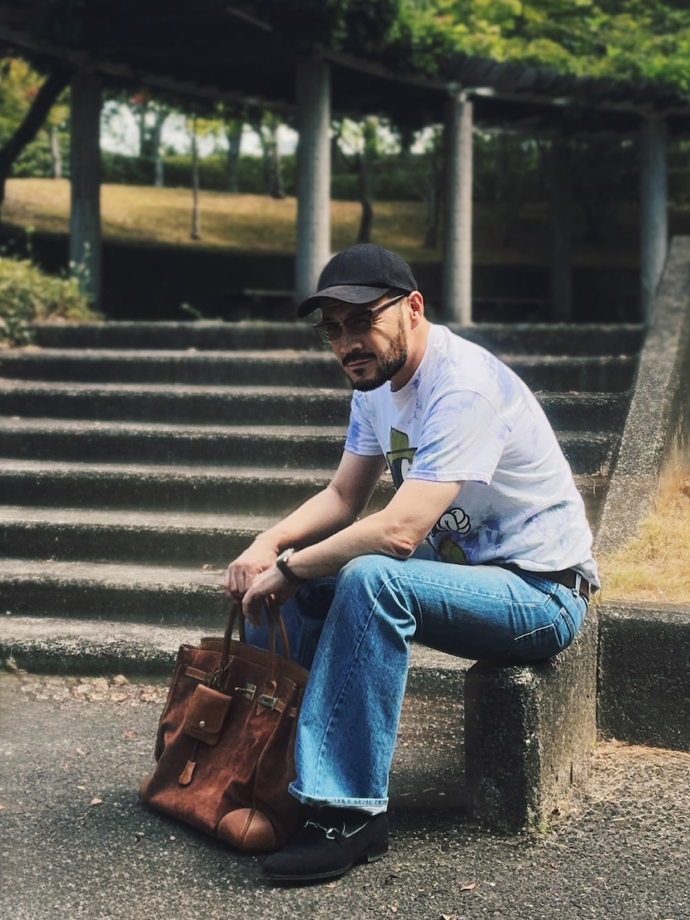 ホワイト系のTシャツ/カットソー、ブルー系のデニムパンツ、ブラウン系のトートバッグを着用したメンズの夏コーディネートの2枚目の写真
