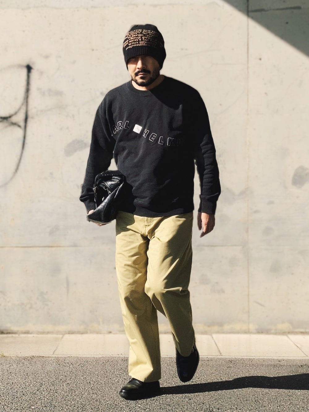 ブラック系のスウェット、ベージュ系のチノパンツ、ブラック系のドレスシューズを着用したメンズの秋コーディネートの2枚目の写真