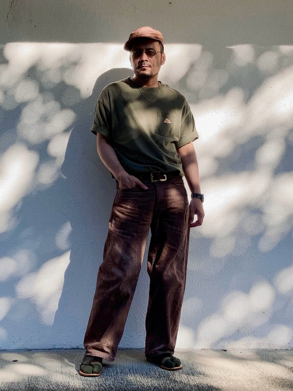 ブラウン系のデニムパンツ、グリーン系のTシャツ/カットソー、ブラウン系のサンダルを着用したメンズの夏コーディネートの2枚目の写真