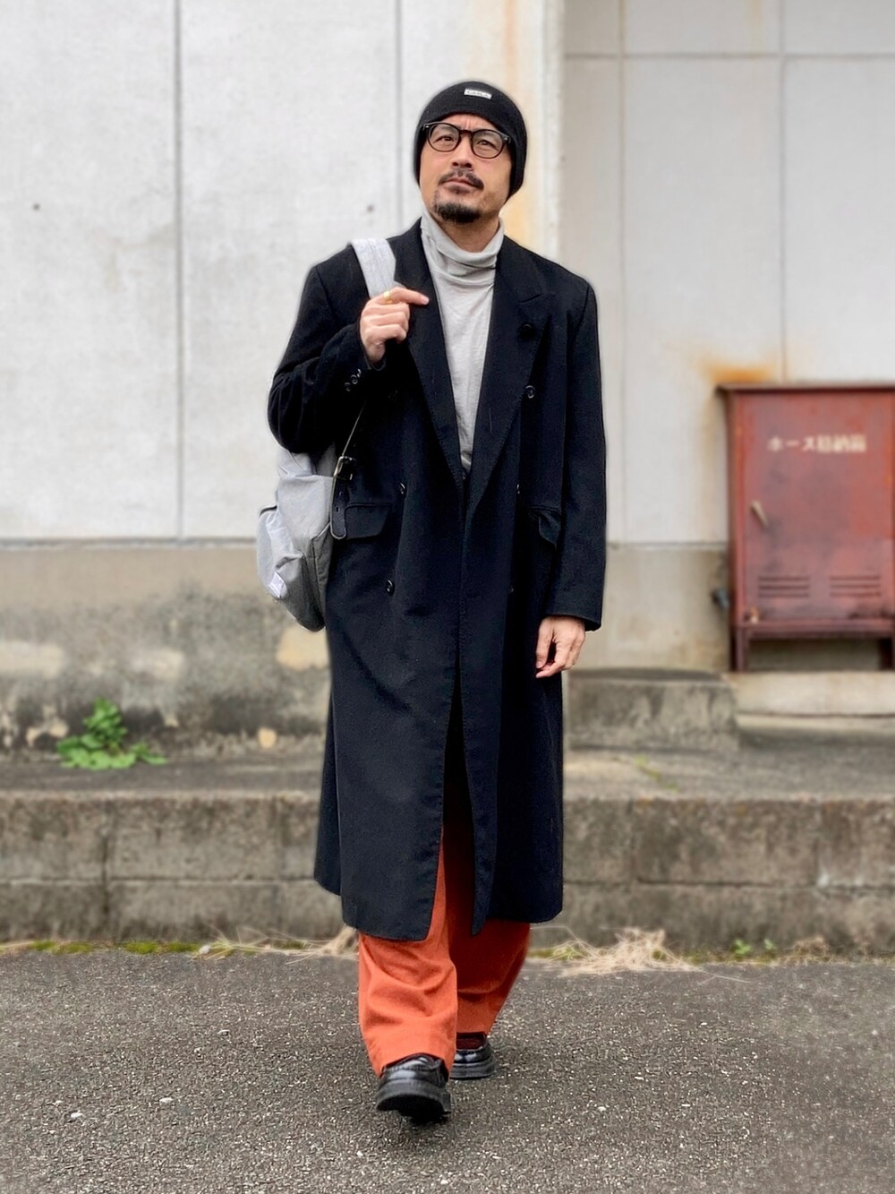 グレー系のTシャツ/カットソー、ブラック系のチェスターコート、オレンジ系のカーゴパンツを着用したメンズの冬コーディネートの4枚目の写真