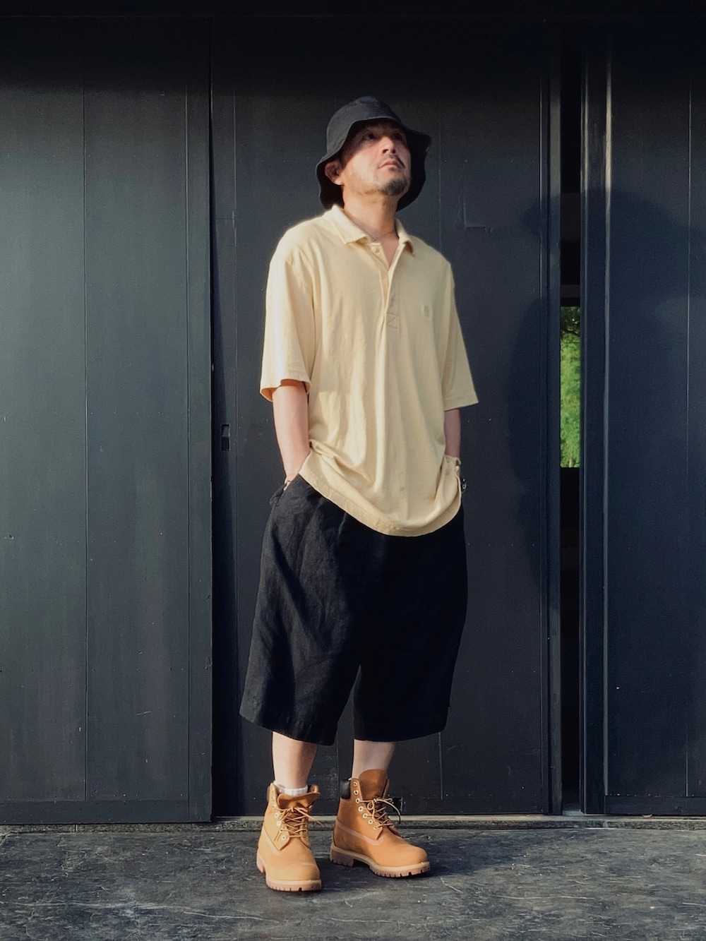 イエロー系のポロシャツ、ブラック系のその他パンツ、イエロー系のブーツを着用したメンズの夏コーディネートの3枚目の写真