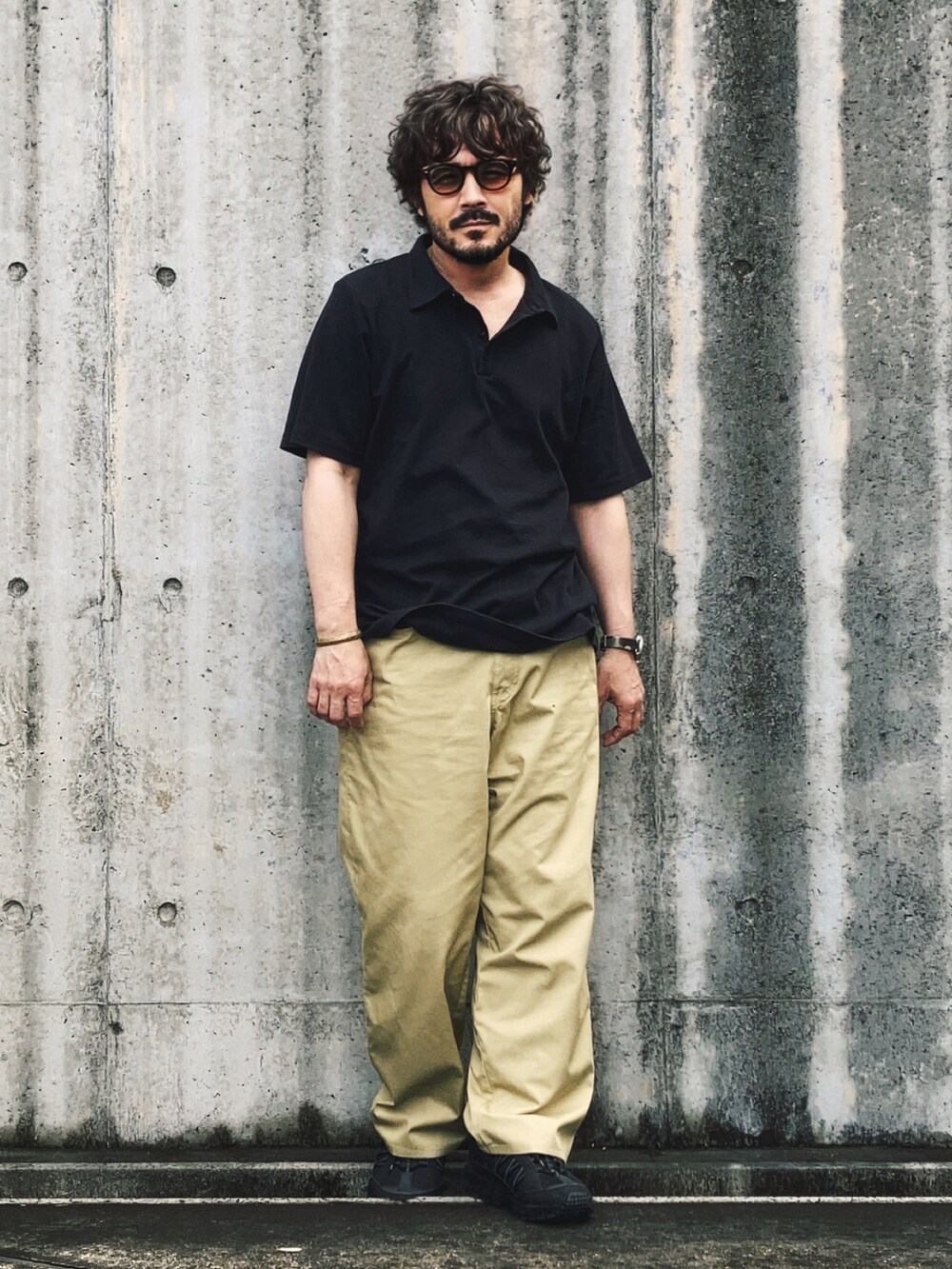 ブラック系のポロシャツ、ベージュ系のチノパンツ、ブラック系のスニーカーを着用したメンズの春コーディネートの2枚目の写真