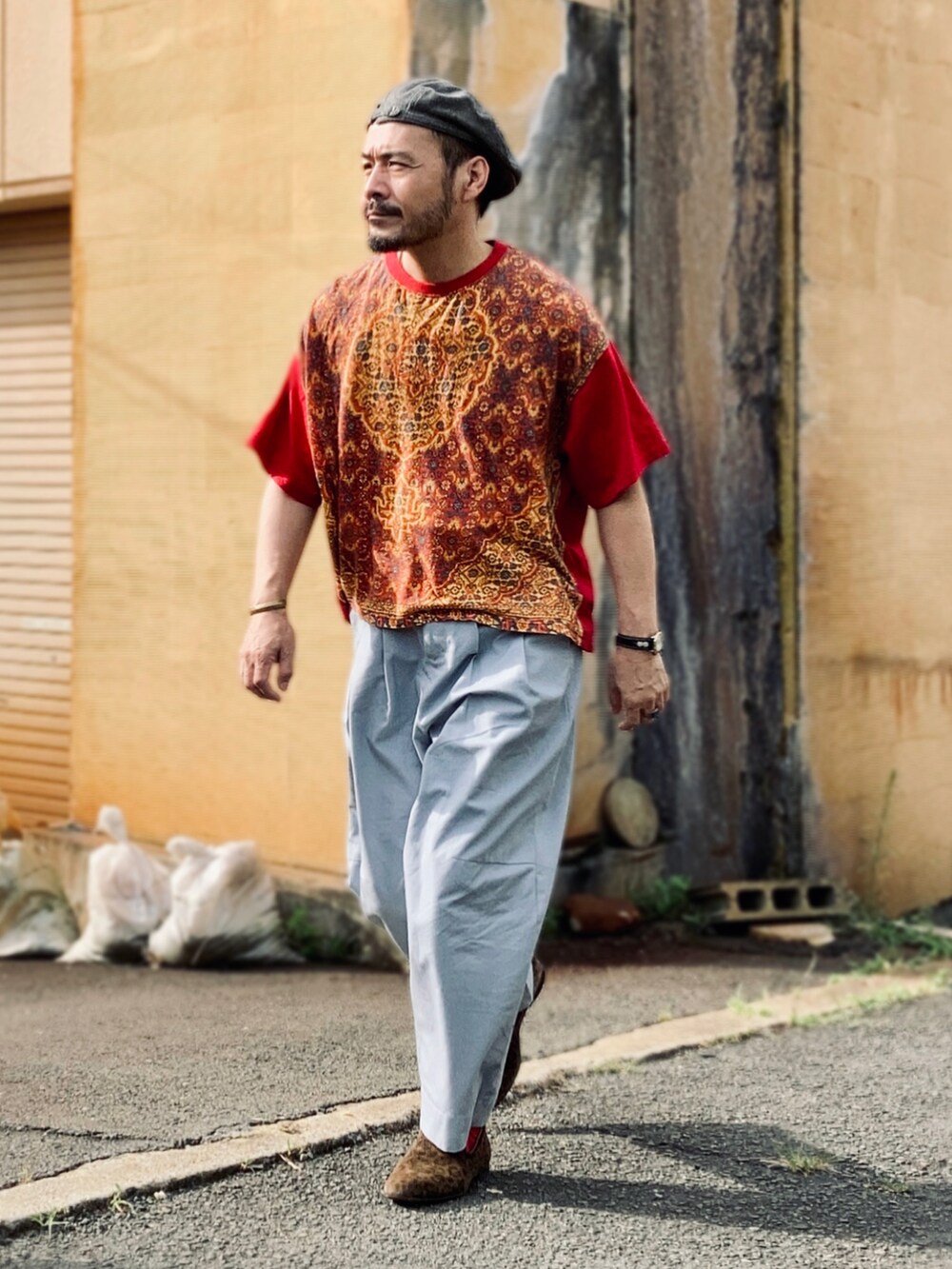 レッド系のTシャツ/カットソー、グレー系のパンツ、ブラウン系のスリッポンを着用したメンズの夏コーディネートの4枚目の写真