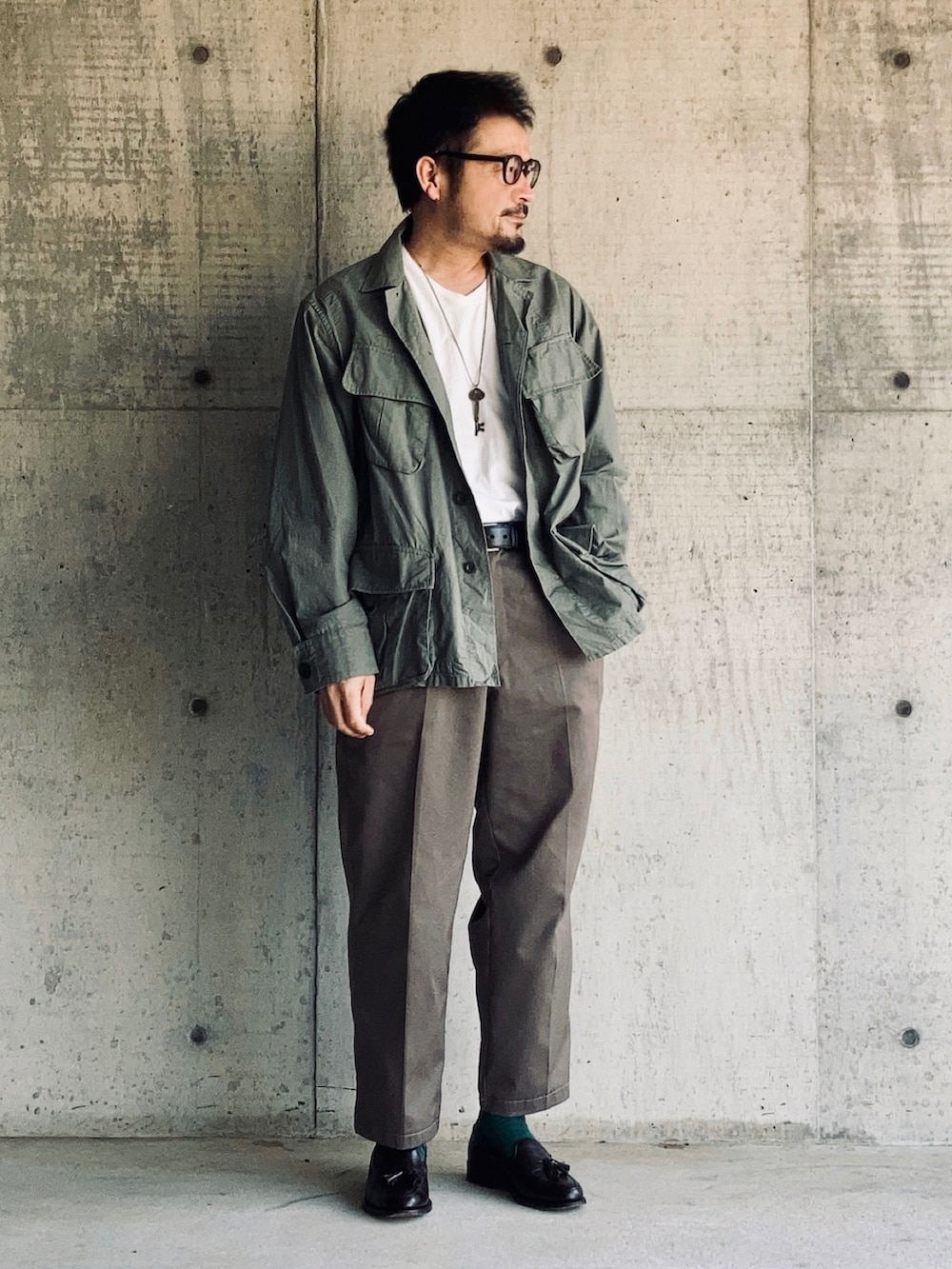 ホワイト系のTシャツ/カットソー、グリーン系のミリタリージャケット、グレー系のスラックスを着用したメンズの春コーディネートの4枚目の写真