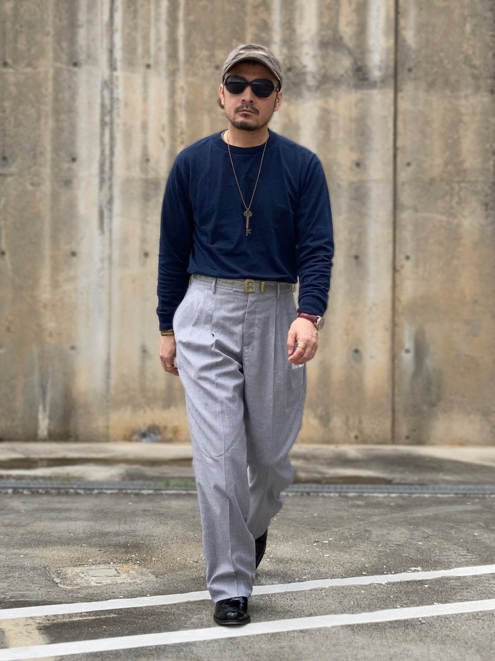 グレー系のスラックス、ブラック系のブーツ、グレー系のキャップを着用したメンズの春コーディネートの2枚目の写真