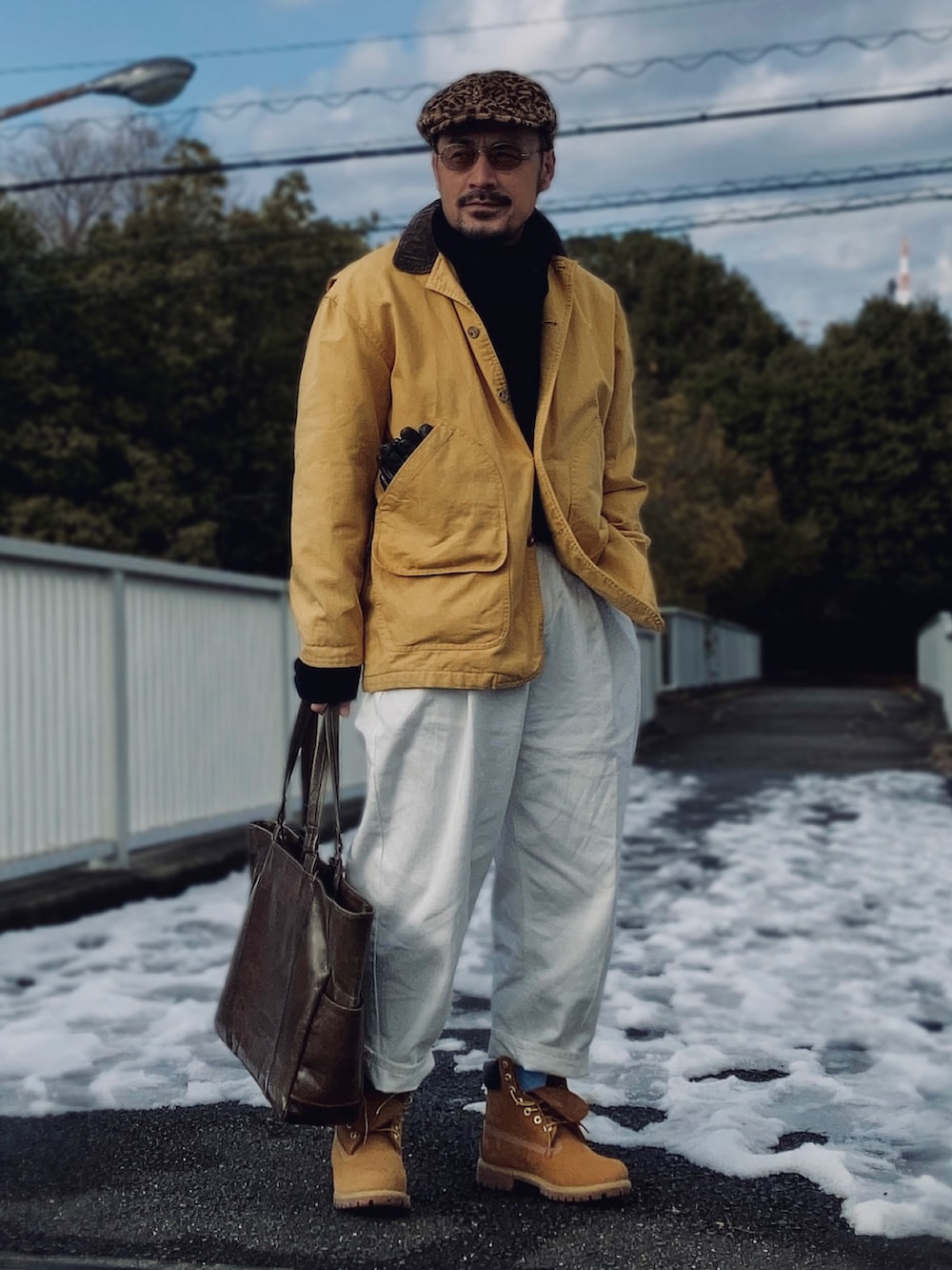 ブラック系のニット/セーター、イエロー系のカバーオール、ホワイト系のスラックスを着用したメンズの冬コーディネートの2枚目の写真