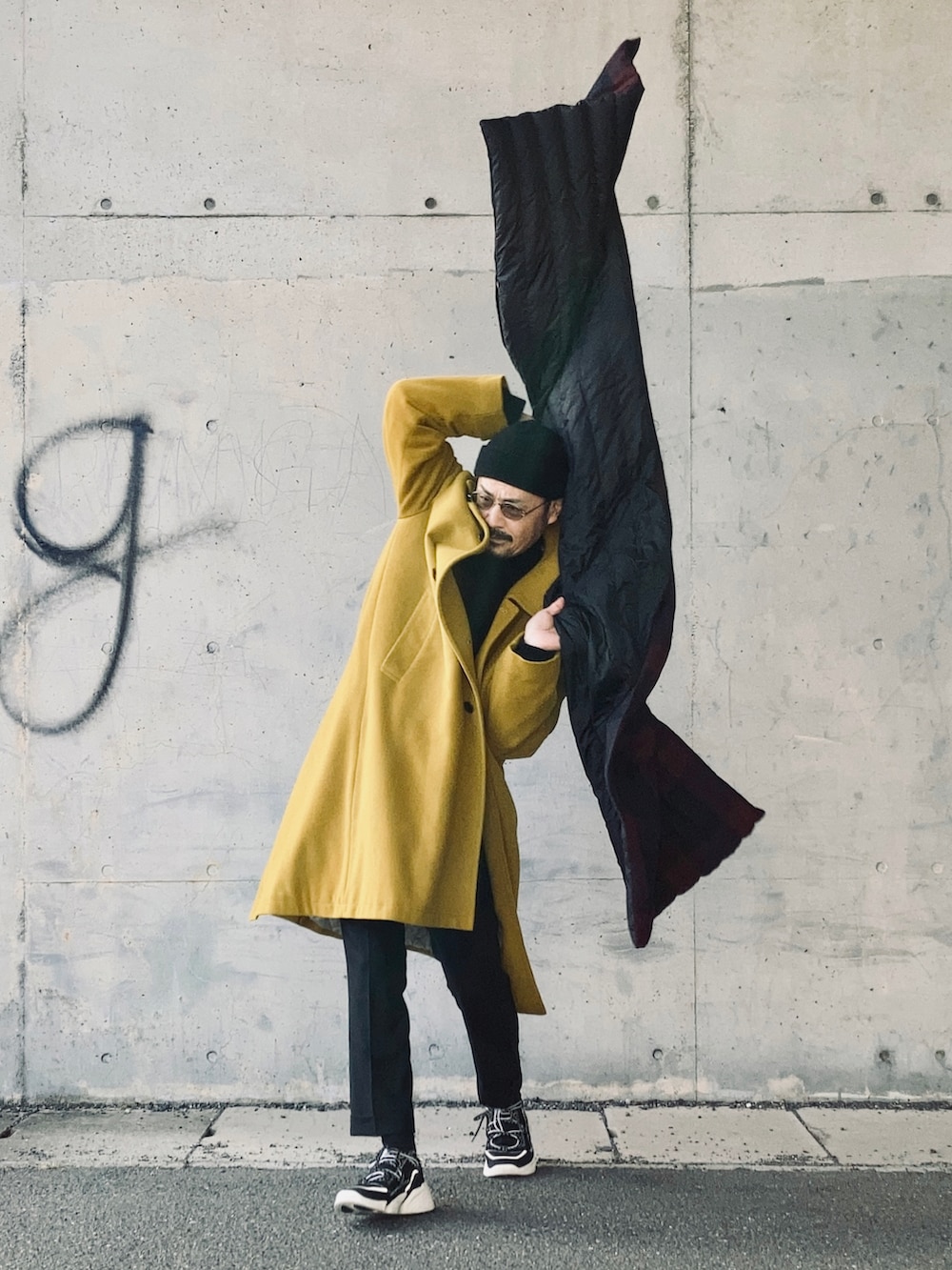 ブラック系のニット/セーター、イエロー系のステンカラーコート、ブラック系のその他パンツを着用したメンズの冬コーディネートの2枚目の写真