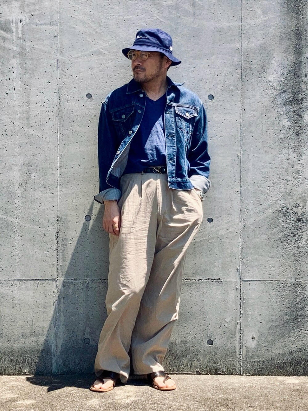 ブルー系のデニムジャケット、ベージュ系のスラックス、ブラウン系のサンダルを着用したメンズの春コーディネートの3枚目の写真