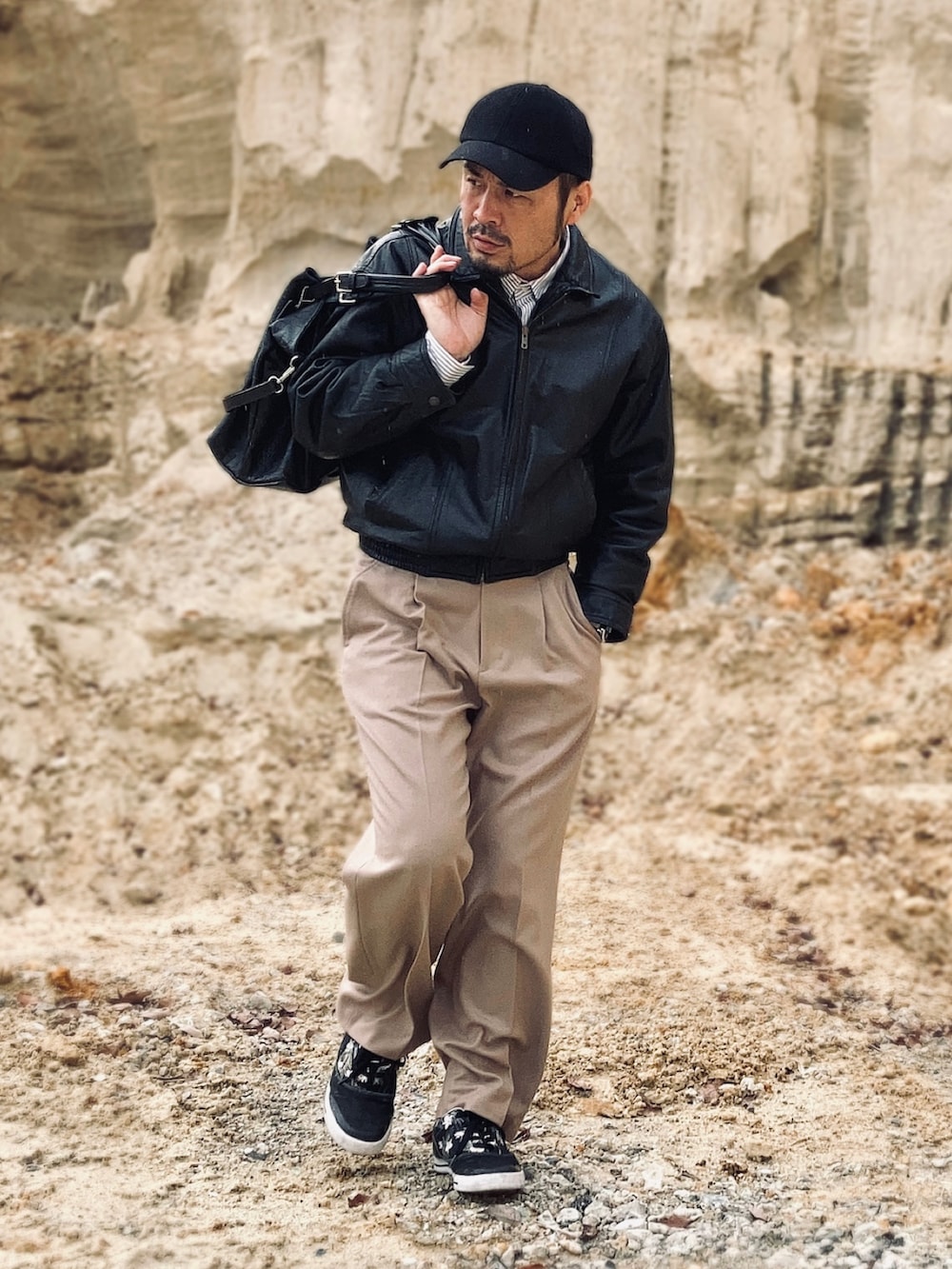 ブラック系のブルゾン、ベージュ系のスラックス、ブラック系のスニーカーを着用したメンズの春コーディネートの2枚目の写真