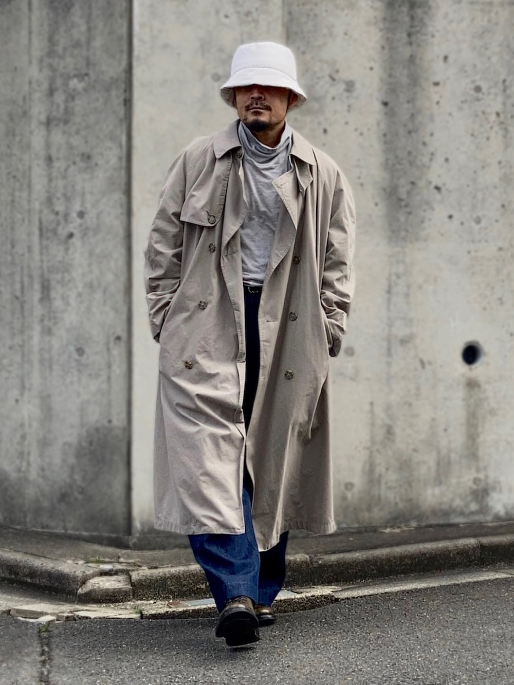 グレー系のTシャツ/カットソー、ベージュ系のトレンチコート、ブルー系のデニムパンツを着用したメンズの春コーディネートの2枚目の写真