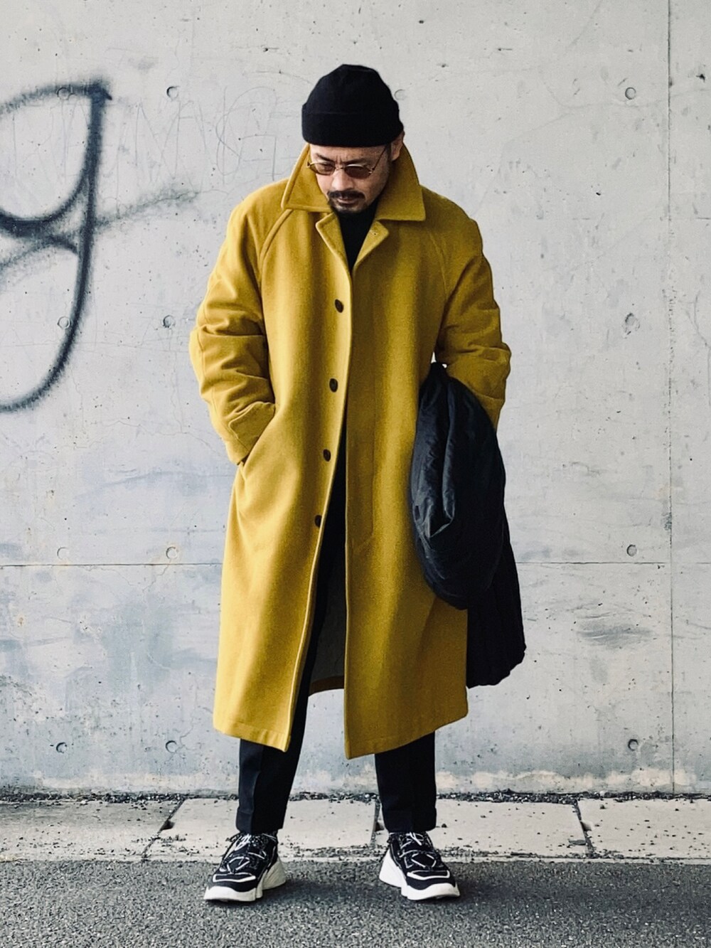 ブラック系のニット/セーター、イエロー系のステンカラーコート、ブラック系のその他パンツを着用したメンズの冬コーディネートの3枚目の写真
