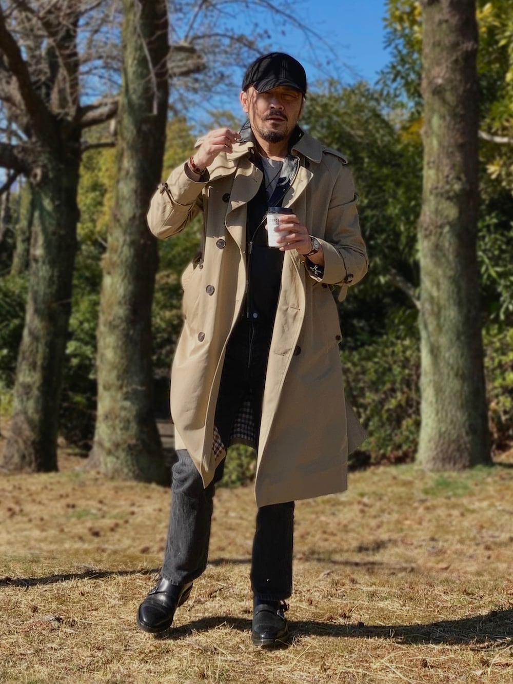 グレー系のTシャツ/カットソー、ブラック系のライダースジャケット、ベージュ系のトレンチコートを着用したメンズの春コーディネートの2枚目の写真