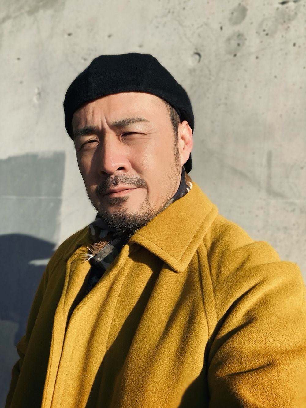 イエロー系のステンカラーコート、ブラック系のスラックス、ブラック系のローファーを着用したメンズの冬コーディネートの4枚目の写真