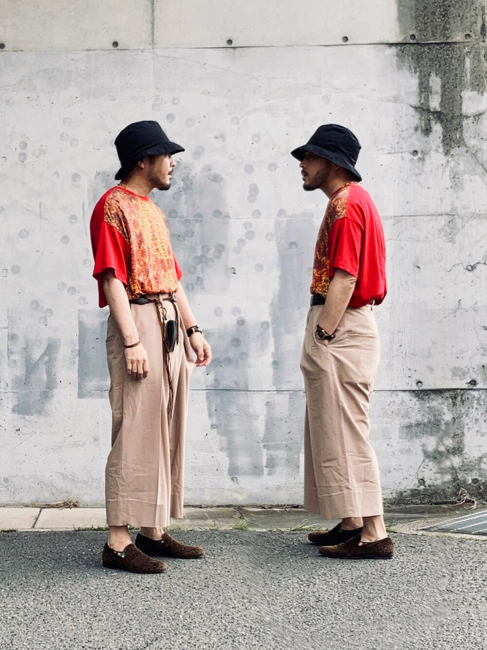 レッド系のTシャツ/カットソー、ベージュ系のスラックス、ブラウン系のスリッポンを着用したメンズの春コーディネートの2枚目の写真