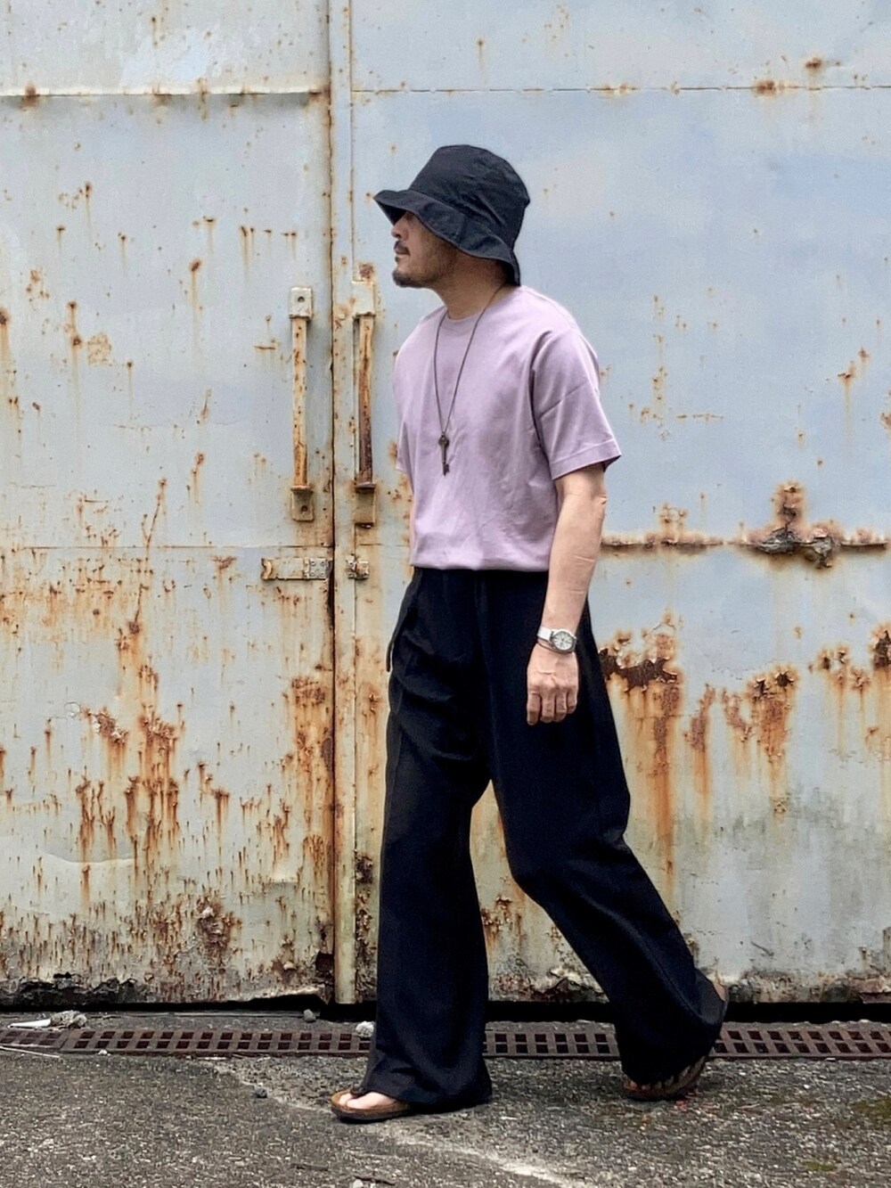 パープル系のTシャツ/カットソー、ブラック系のスラックス、ブラック系のサンダルを着用したメンズの春コーディネートの3枚目の写真