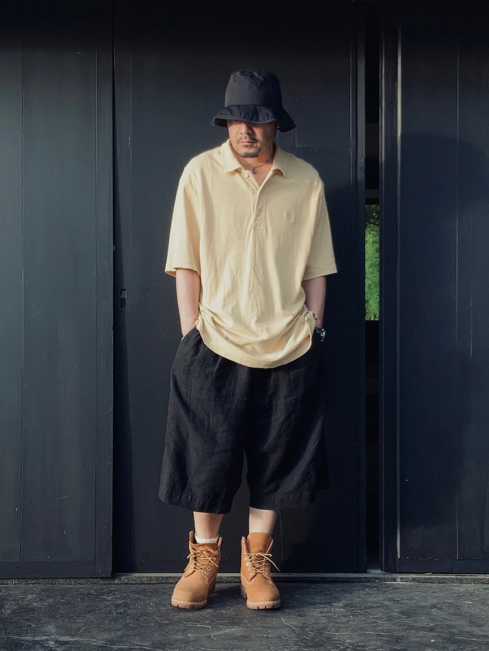 イエロー系のポロシャツ、ブラック系のその他パンツ、イエロー系のブーツを着用したメンズの夏コーディネートの2枚目の写真