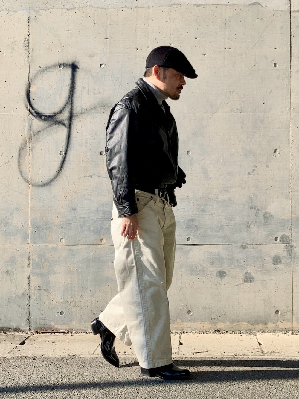 グレー系のニット/セーター、ブラック系のブルゾン、ホワイト系のデニムパンツを着用したメンズの冬コーディネートの3枚目の写真