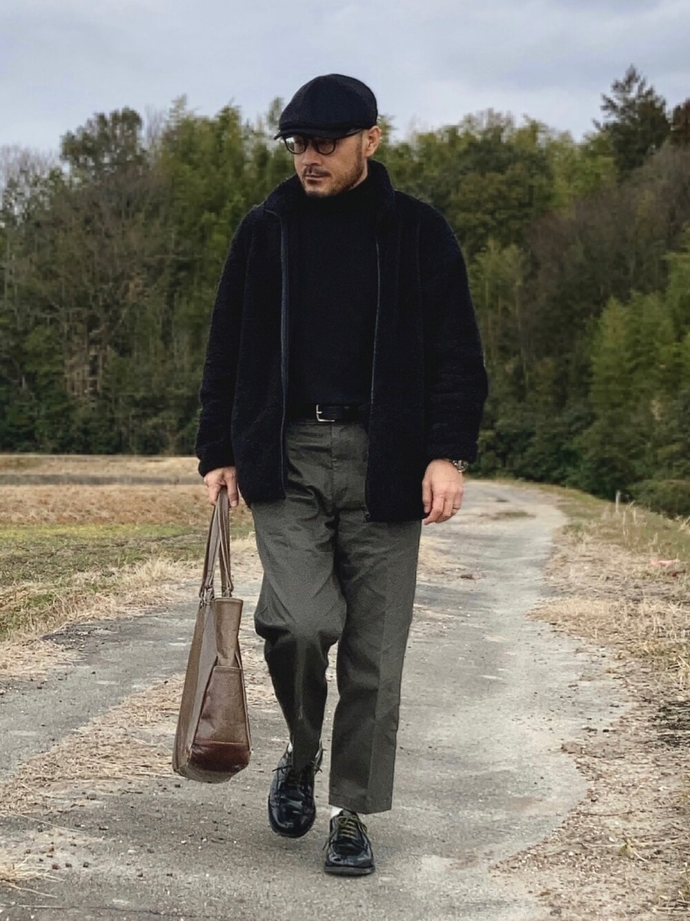 ブラック系のニット/セーター、ブラック系のその他アウター、グリーン系のチノパンツを着用したメンズの冬コーディネートの2枚目の写真