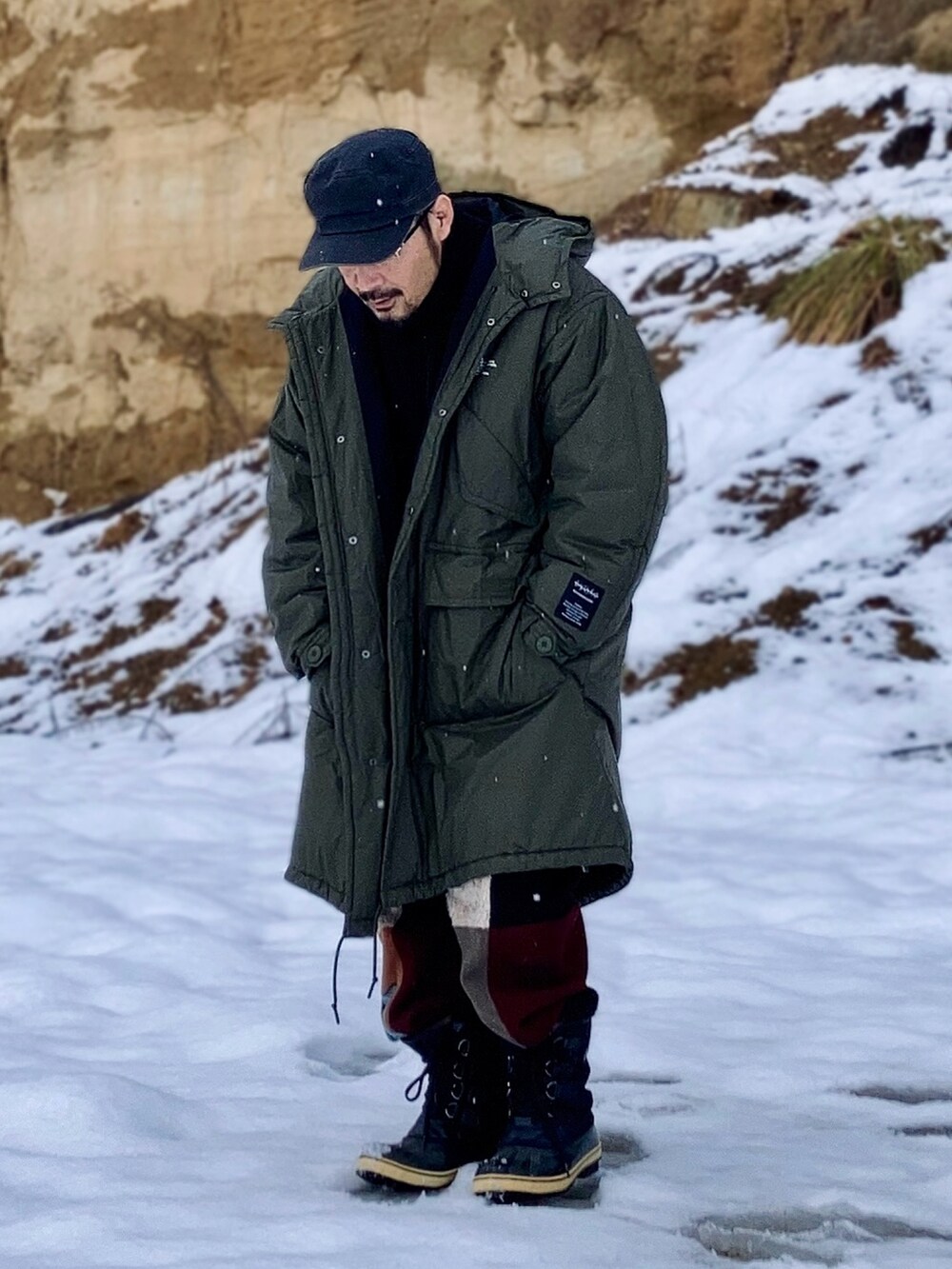 グリーン系のミリタリージャケット、ブラック系のその他アウター、その他のスウェットパンツを着用したメンズの冬コーディネートの3枚目の写真