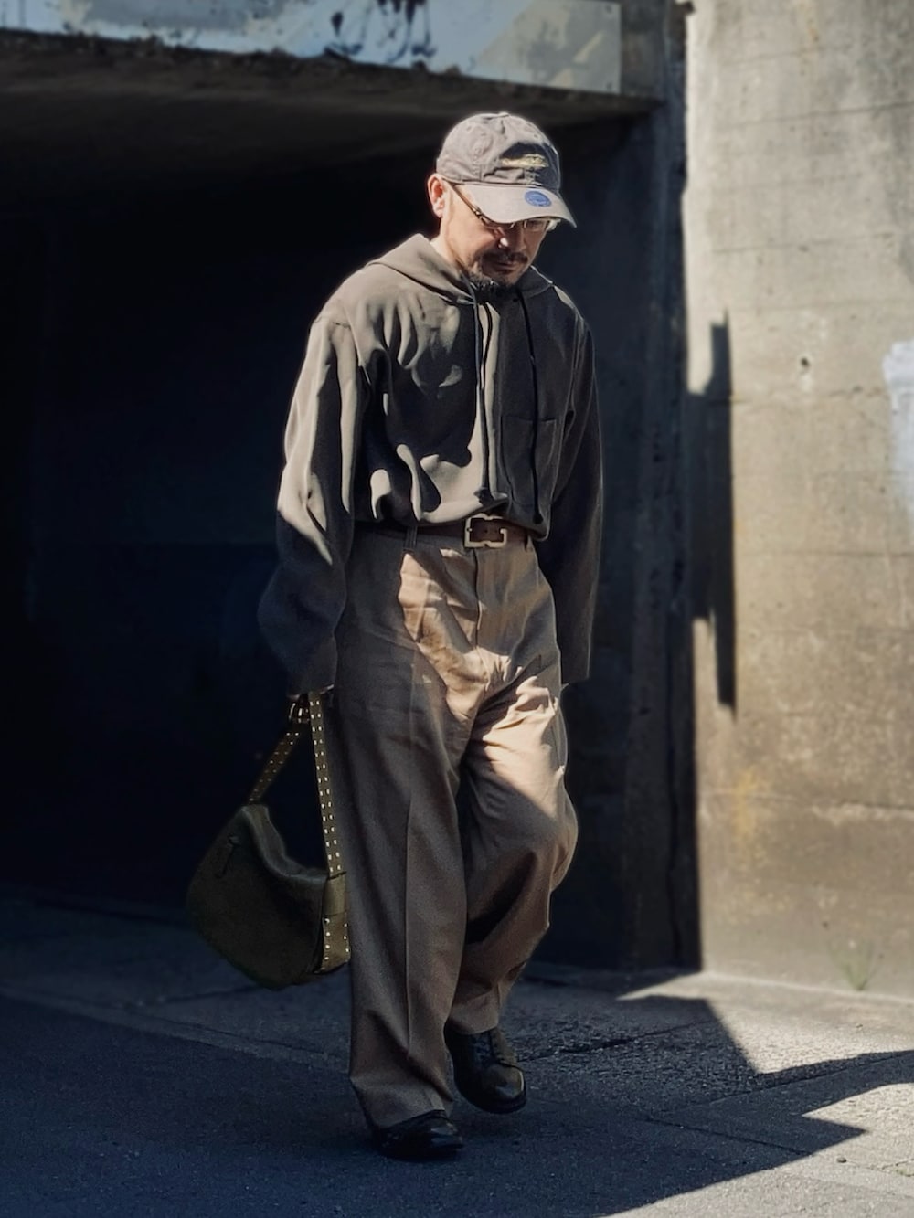 グレー系のパーカー、ベージュ系のスラックス、グリーン系のブーツを着用したメンズの春コーディネートの2枚目の写真