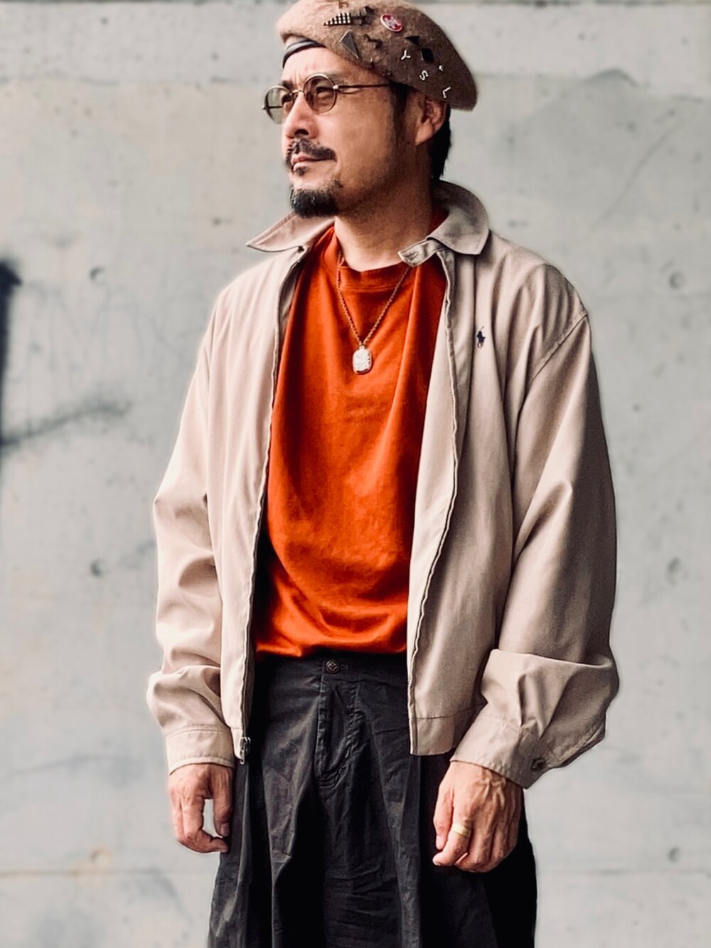 オレンジ系のTシャツ/カットソー、ベージュ系のブルゾン、ブラウン系のパンツを着用したメンズの秋コーディネートの3枚目の写真