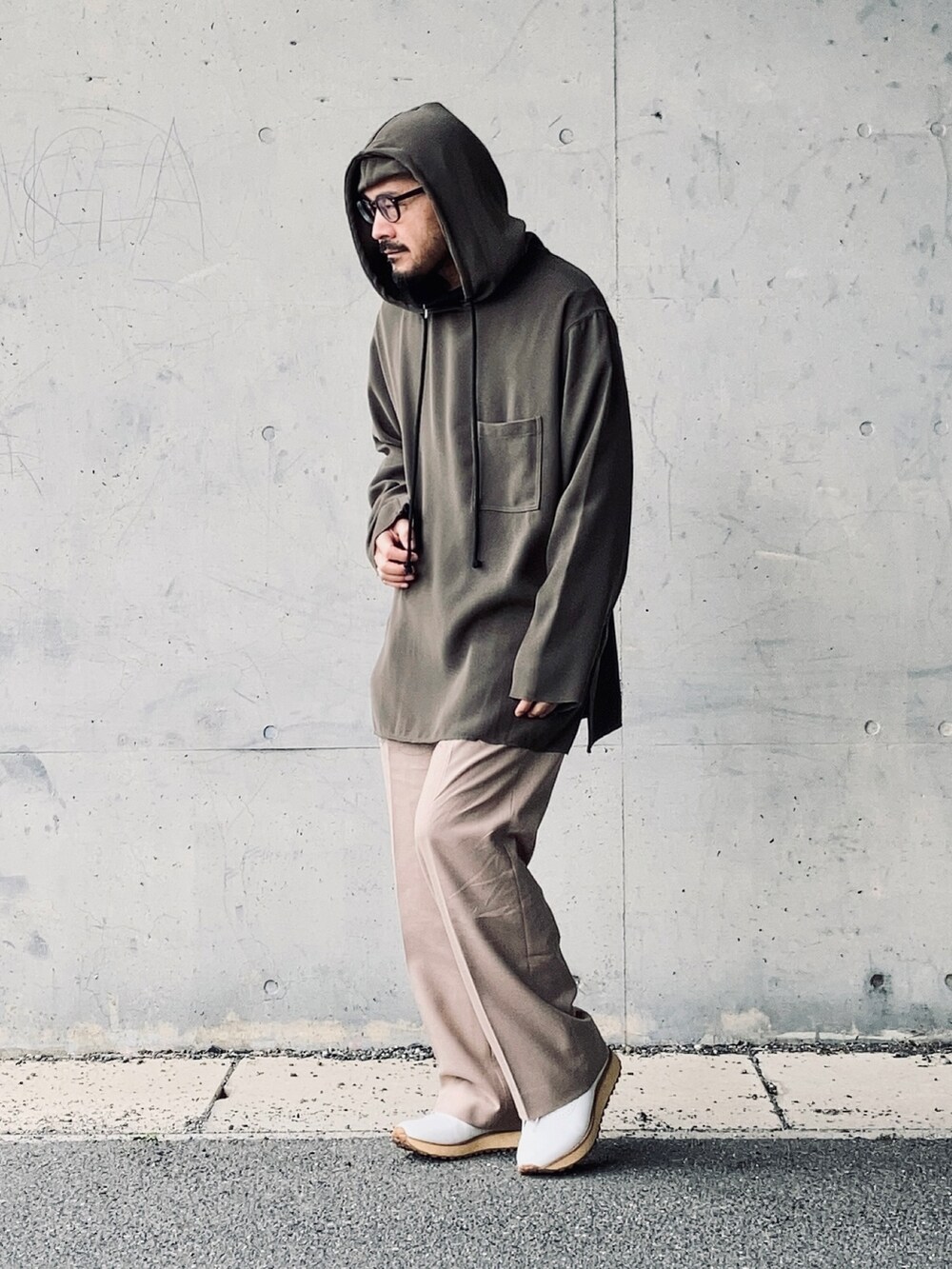 ブラック系のニット/セーター、グレー系のパーカー、ベージュ系のスラックスを着用したメンズの春コーディネートの3枚目の写真