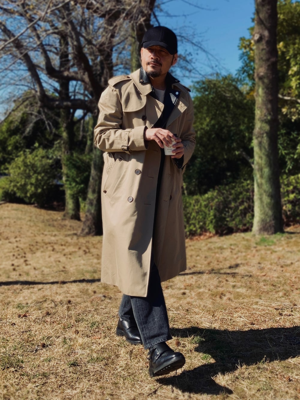 グレー系のTシャツ/カットソー、ブラック系のライダースジャケット、ベージュ系のトレンチコートを着用したメンズの春コーディネートの3枚目の写真