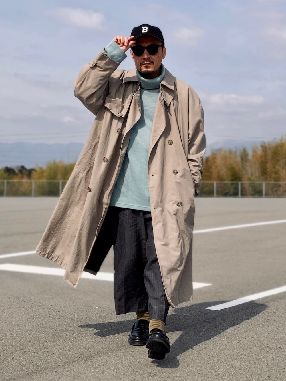 ブルー系のニット/セーター、ベージュ系のトレンチコート、グレー系のスラックスを着用したメンズの春コーディネートの3枚目の写真
