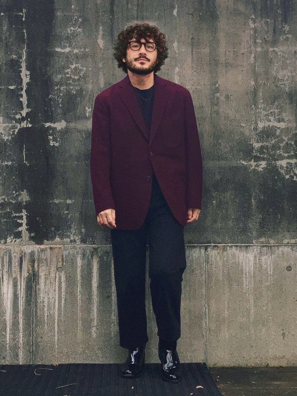 レッド系のテーラードジャケット、ブラック系のパンツ、ブラック系のブーツを着用したメンズの秋コーディネートの3枚目の写真