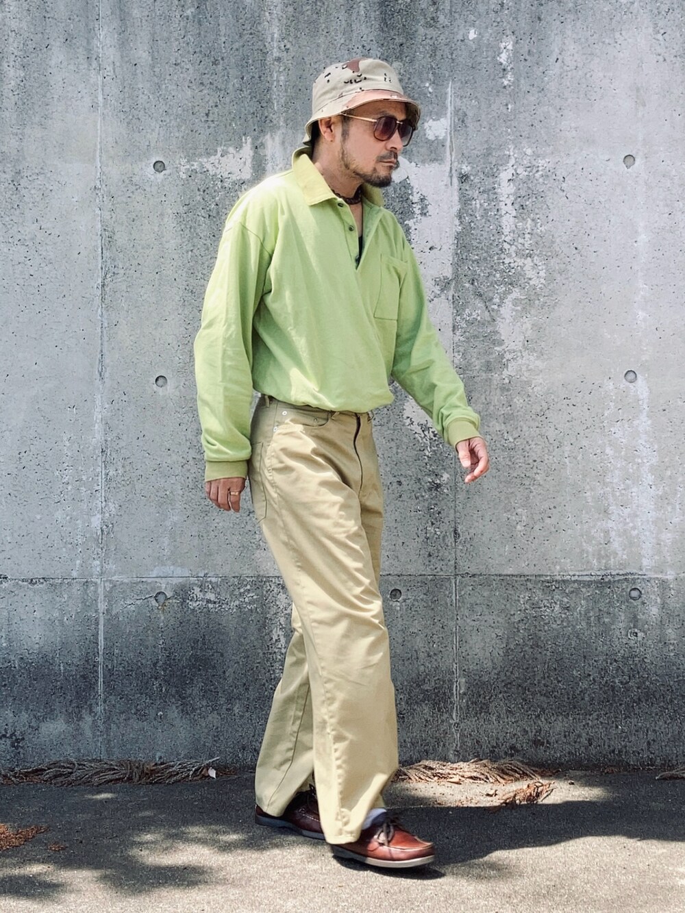 グリーン系のポロシャツ、ベージュ系のチノパンツ、ブラウン系のモカシン/デッキシューズを着用したメンズの春コーディネートの2枚目の写真