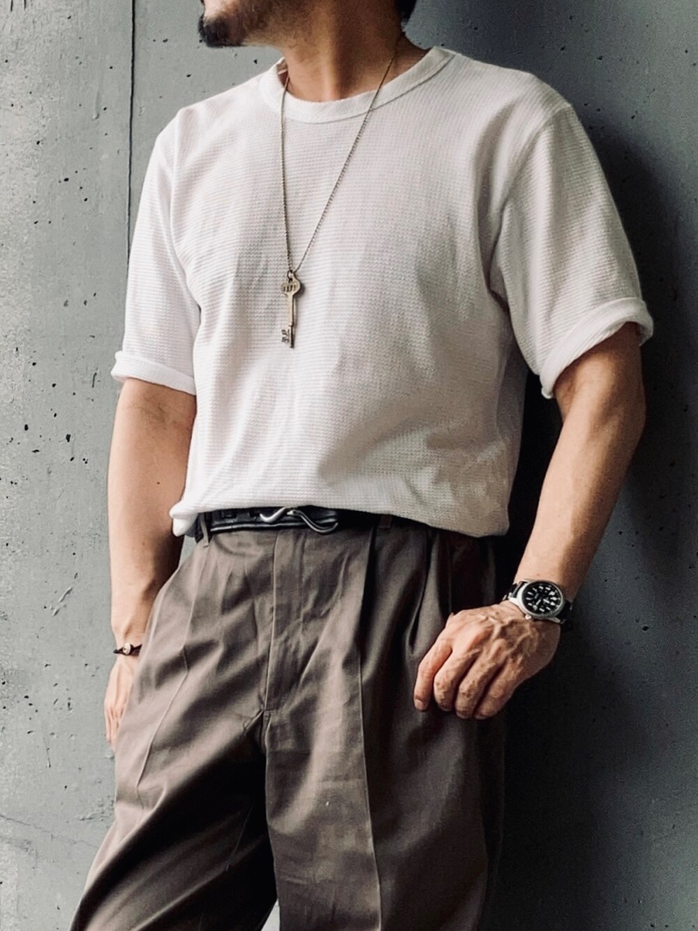 ホワイト系のTシャツ/カットソー、グレー系のスラックス、ブラック系のサンダルを着用したメンズの夏コーディネートの2枚目の写真