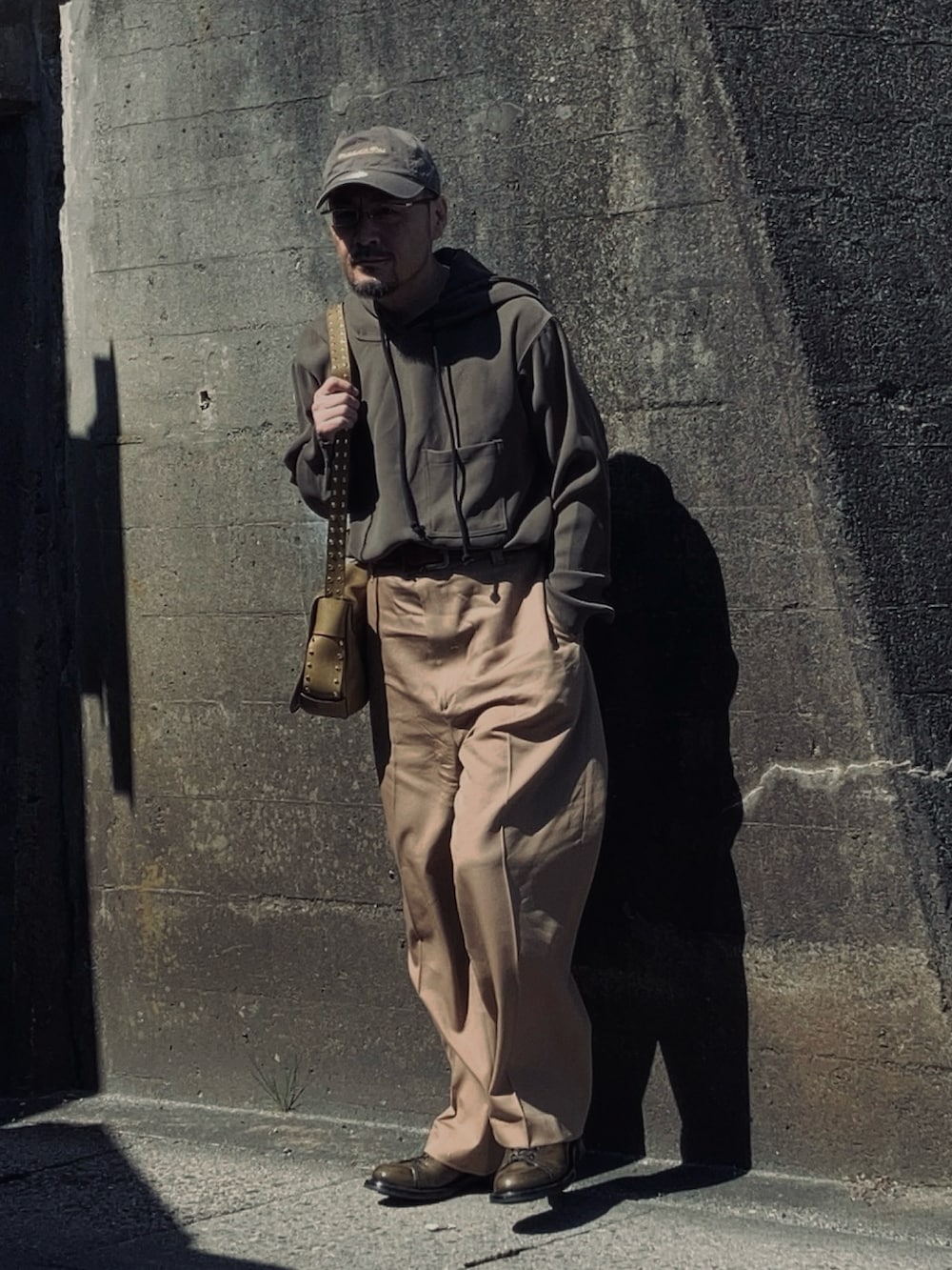 グレー系のパーカー、ベージュ系のスラックス、グリーン系のブーツを着用したメンズの春コーディネートの3枚目の写真