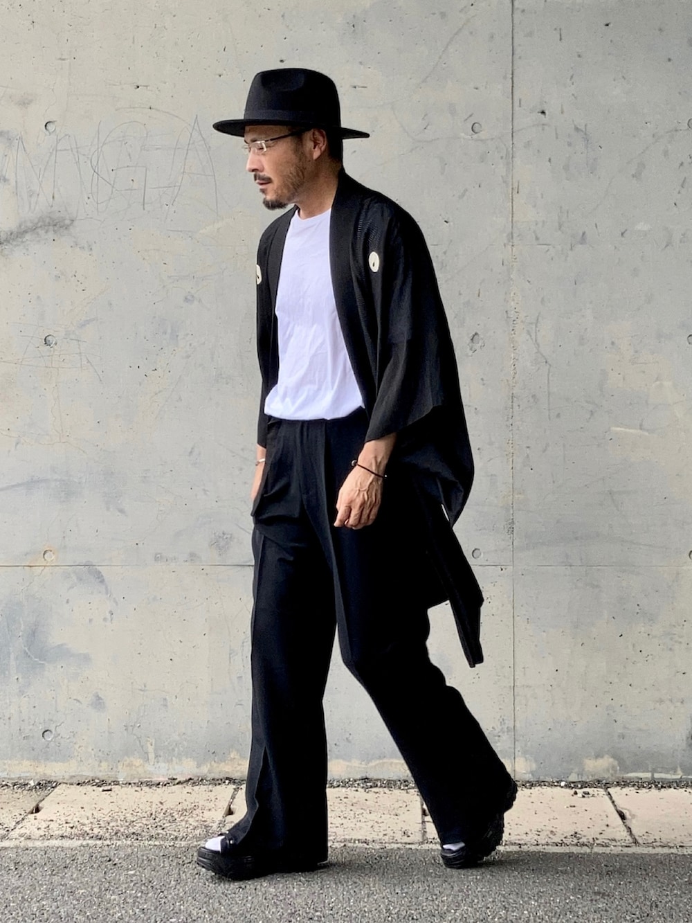ホワイト系のTシャツ/カットソー、ブラック系のスラックス、ブラック系のサンダルを着用したメンズの夏コーディネートの3枚目の写真