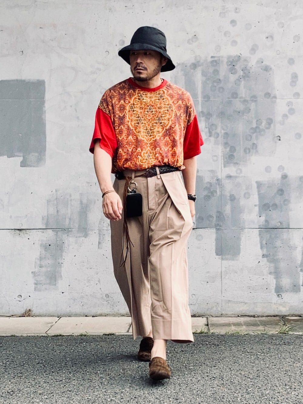 レッド系のTシャツ/カットソー、ベージュ系のスラックス、ブラウン系のスリッポンを着用したメンズの春コーディネートの3枚目の写真