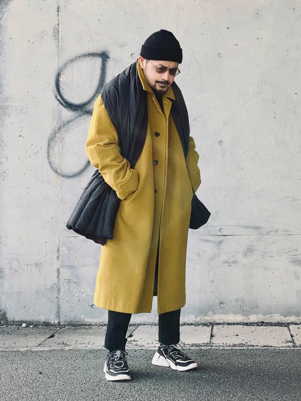 ブラック系のニット/セーター、イエロー系のステンカラーコート、ブラック系のその他パンツを着用したメンズの冬コーディネートの4枚目の写真