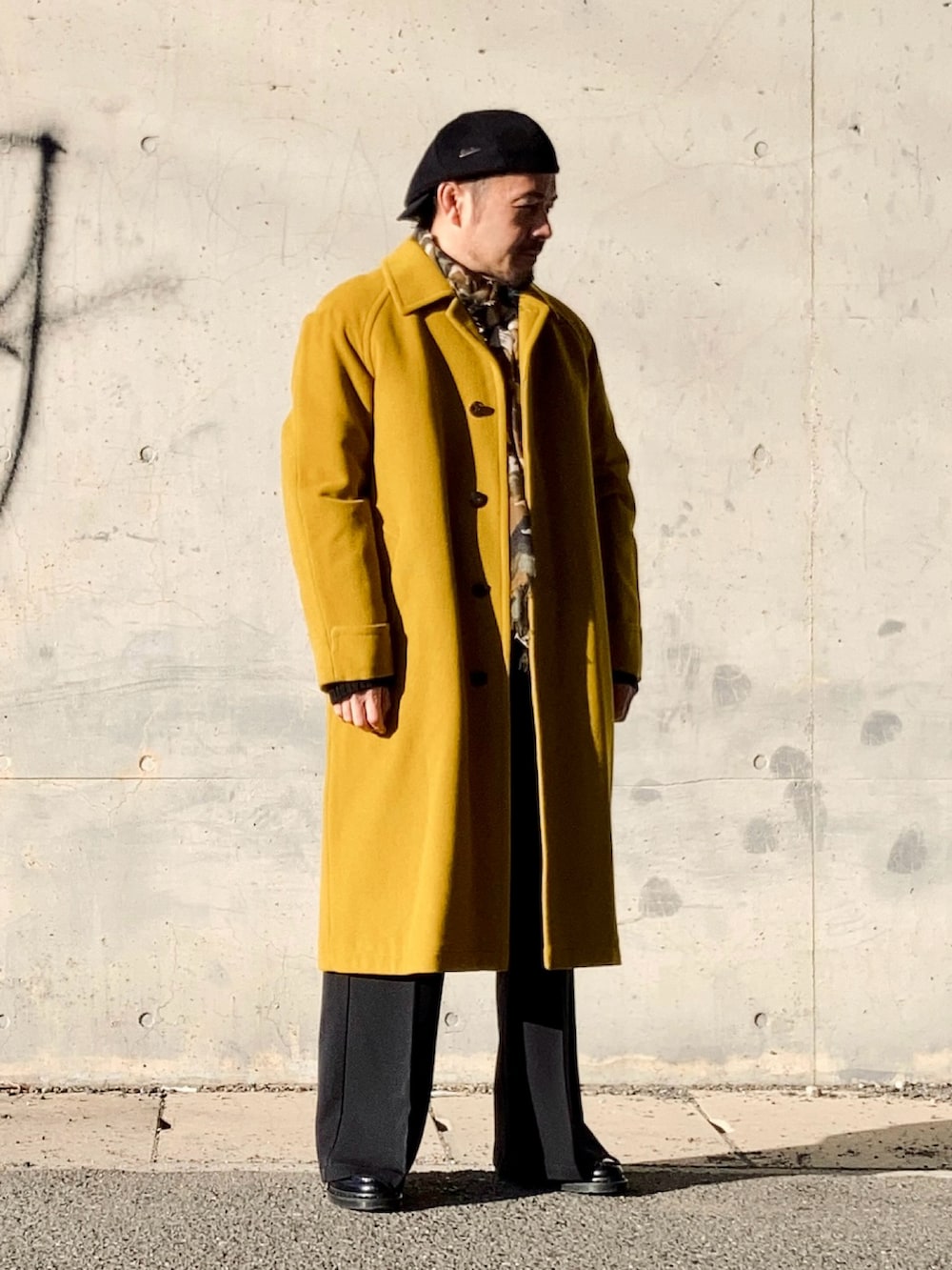イエロー系のステンカラーコート、ブラック系のスラックス、ブラック系のローファーを着用したメンズの冬コーディネートの3枚目の写真