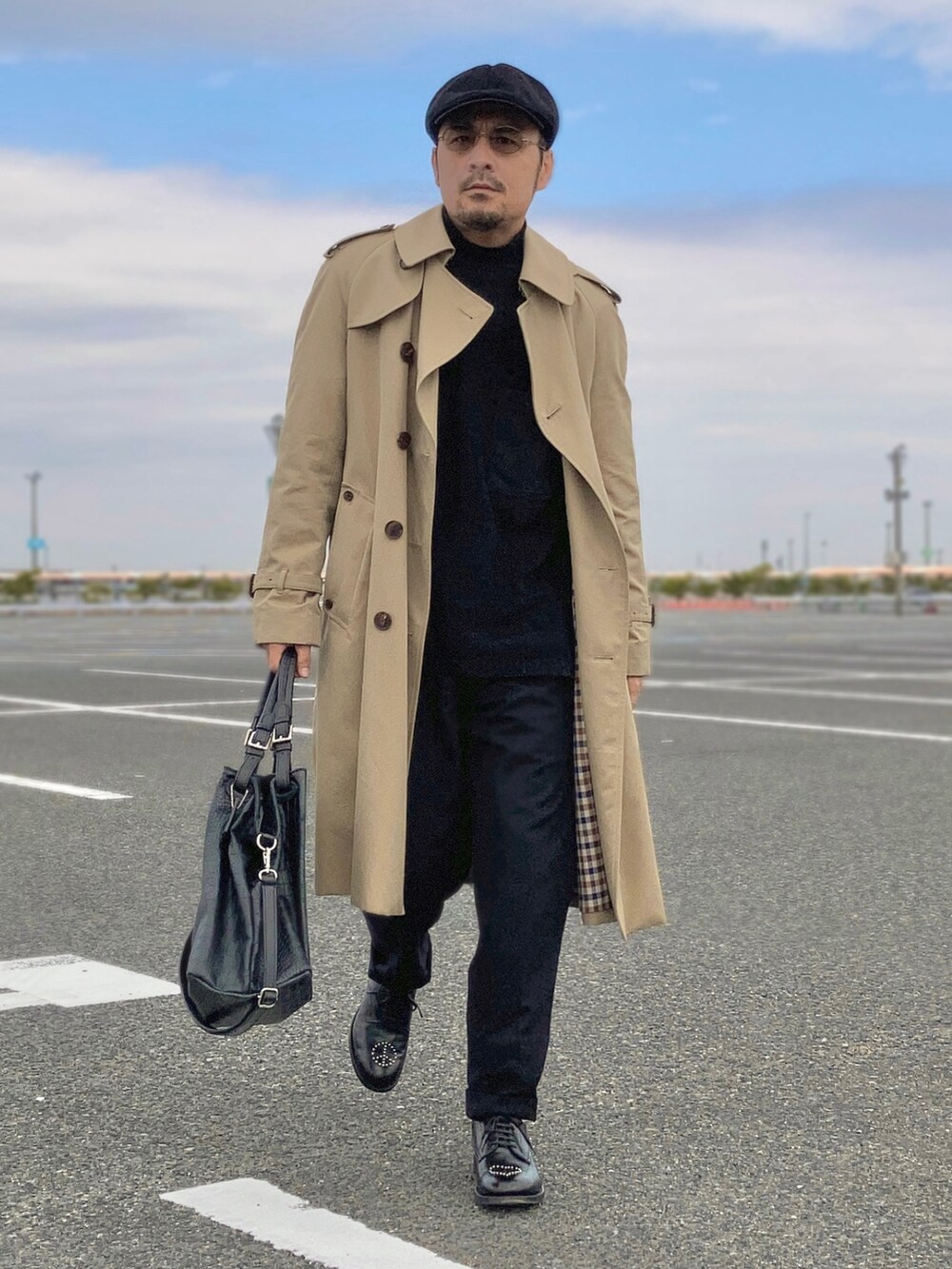 ブラック系のニット/セーター、ベージュ系のトレンチコート、ブラック系のスラックスを着用したメンズの秋コーディネートの3枚目の写真