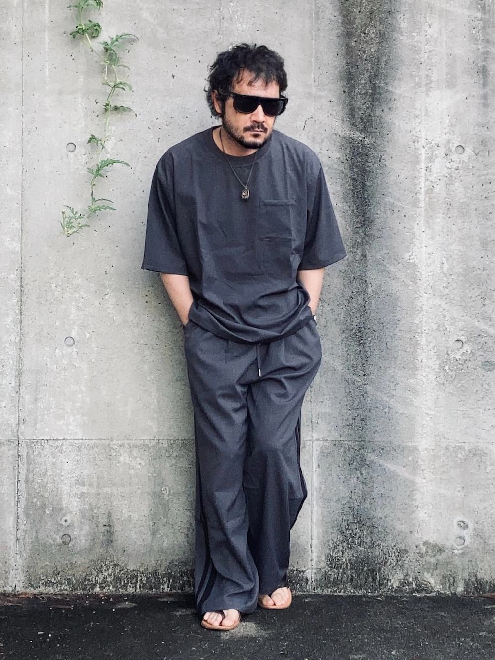 グレー系のTシャツ/カットソー、グレー系のスラックス、ブラウン系のサンダルを着用したメンズの夏コーディネートの2枚目の写真