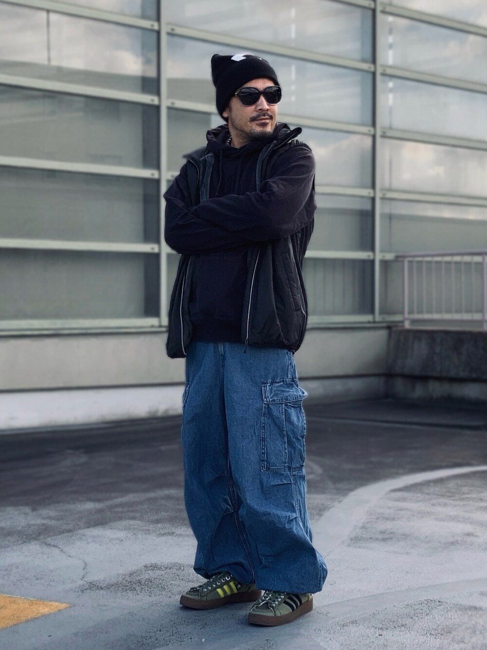 ブラック系のパーカー、ブラック系のベスト、ブルー系のカーゴパンツを着用したメンズの冬コーディネートの3枚目の写真