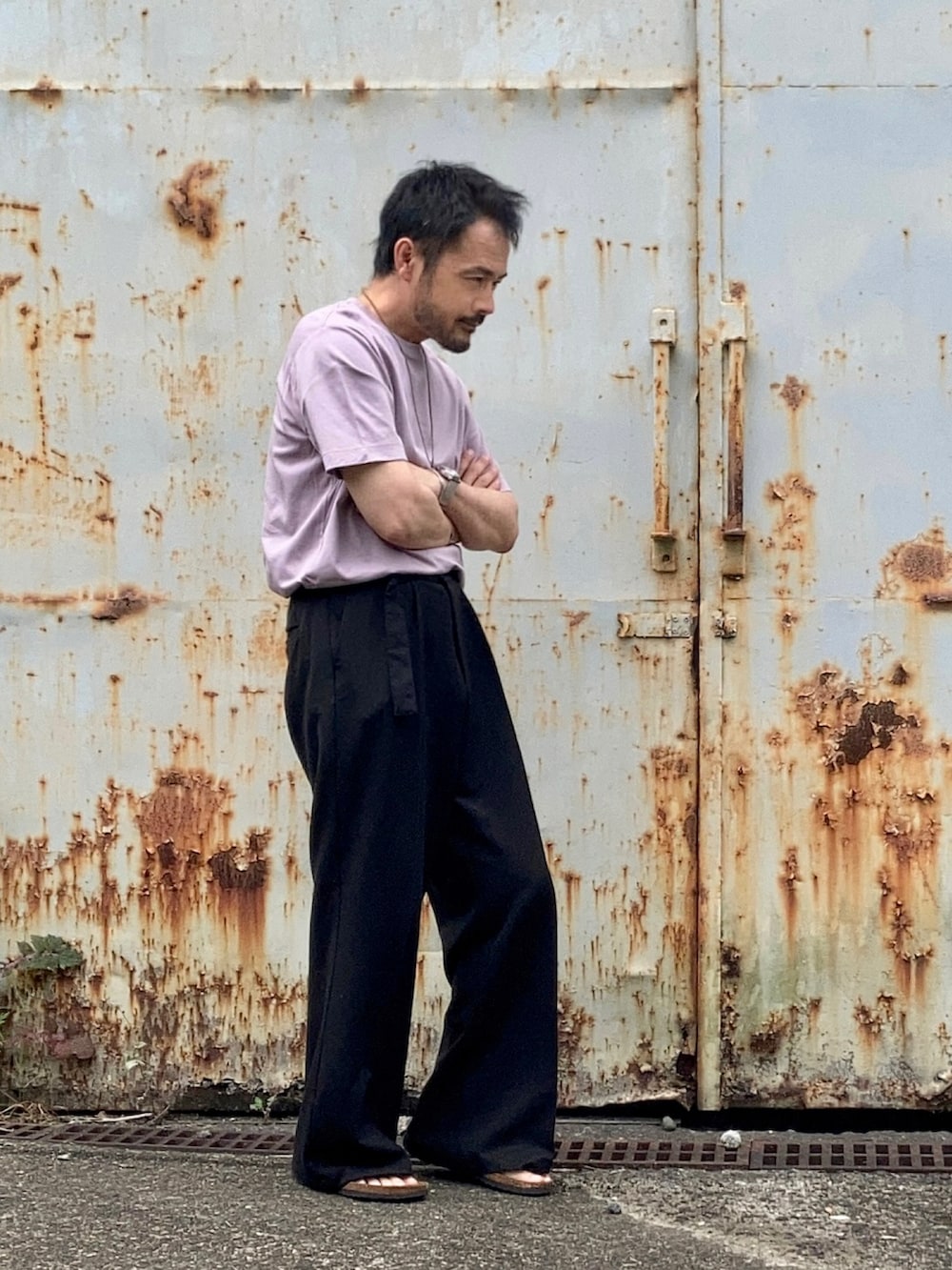 パープル系のTシャツ/カットソー、ブラック系のスラックス、ブラック系のサンダルを着用したメンズの春コーディネートの4枚目の写真