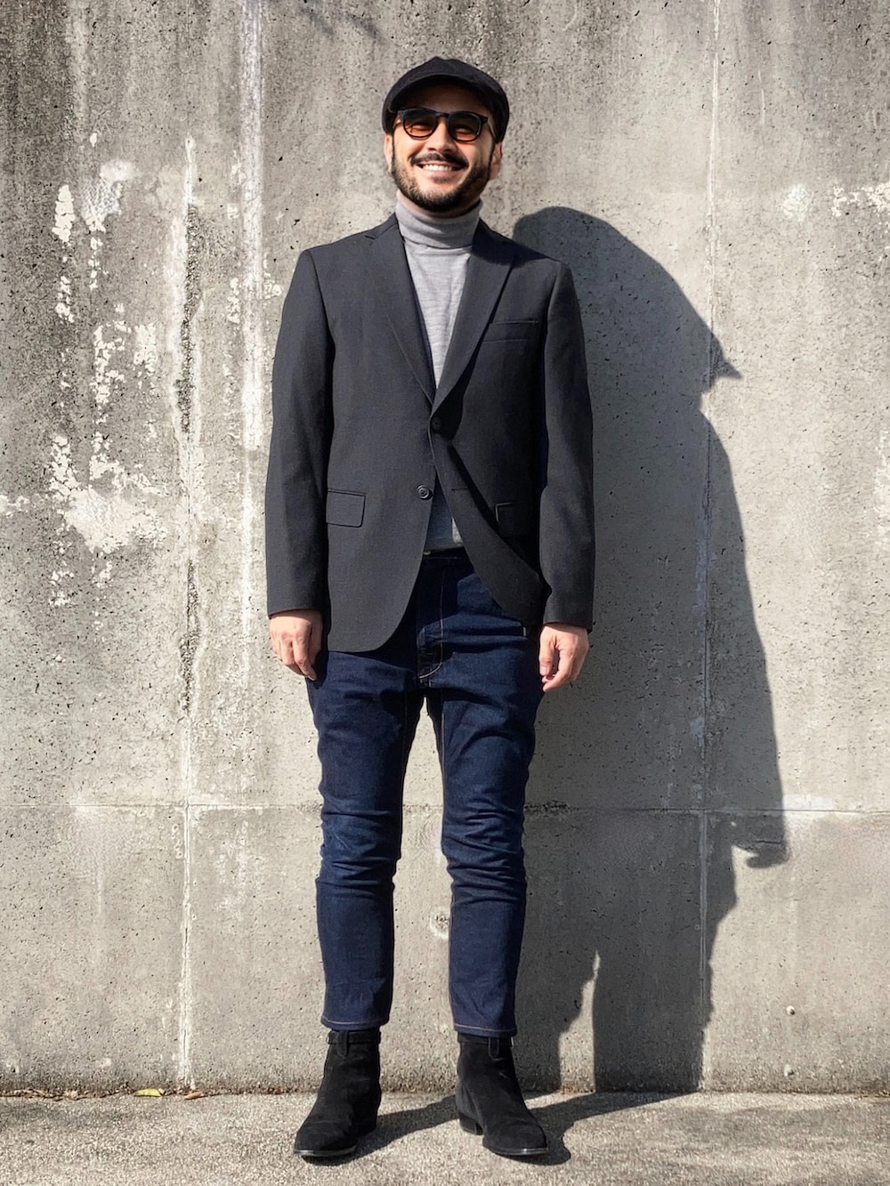 グレー系のテーラードジャケット、ブラック系のブーツ、ブルー系のデニムパンツを着用したメンズの秋コーディネートの2枚目の写真